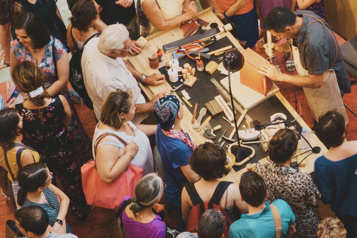 A craftsman from Hermès, surrounded by people, working on a leather bag. Image Anthony Nelzin-Santos.