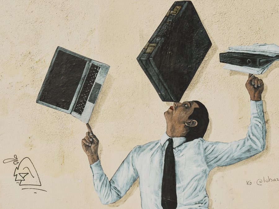 A mural of an office worker juggling a compter, a briefcase, and a stack of papers. Image Anthony Nelzin-Santos.