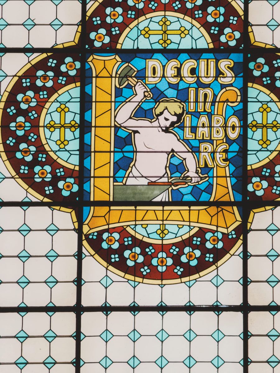A stained glass window featuring the Latin words “decus in labore” (dignity in work). Image Anthony Nelzin-Santos.